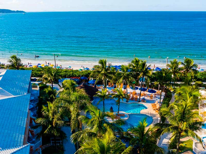 Área da piscina do Vila do Farol, dica de hotel em Bombinhas, SC, em frente à praia em dia de céu azul