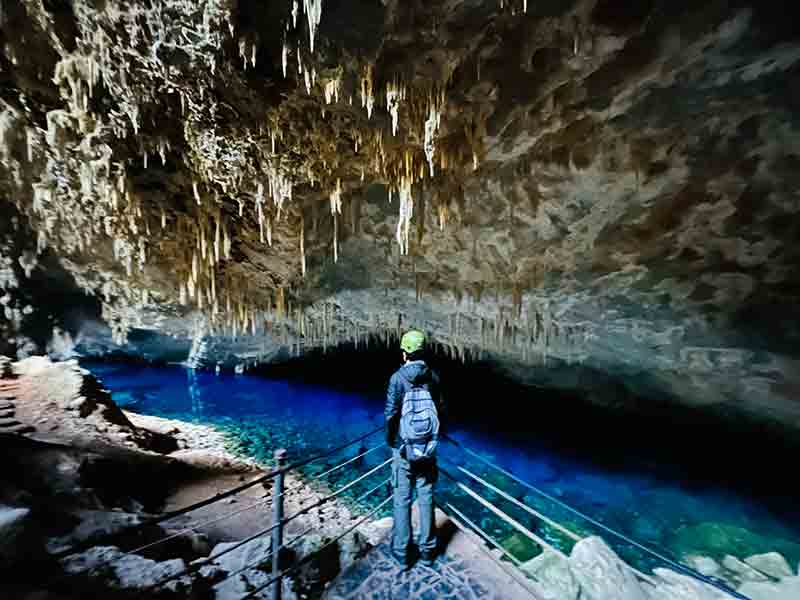 Homem em pé dentro da Gruta do Lago Azul observa o lago cristalino