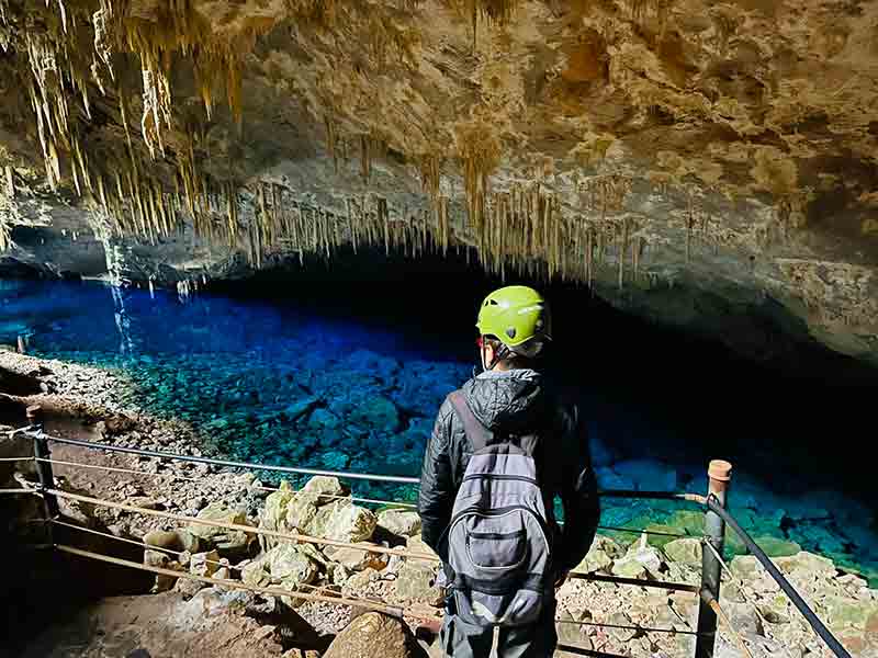 Homem de capacete e mochila dentro da Gruta do Lago Azul, um dos passeios em Bonito, observa a agua cristalina