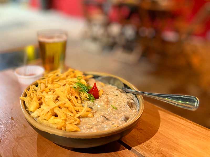 Arroz Carrteiro cremoso com mandioca palha e cerveja ao fundo no Boteco Juanita, em Bonito, MS