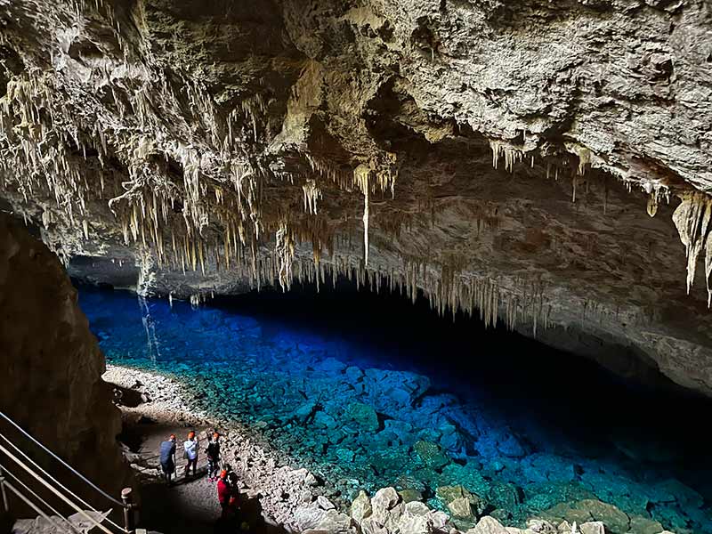 Pessoas dentro da Gruta do Lago Azul observam a água cristalina