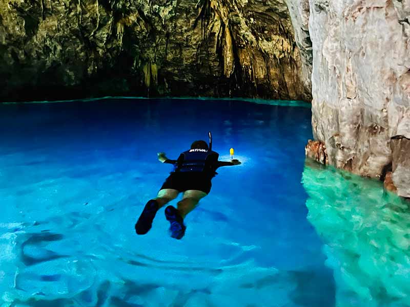 Homem flutua com colete salva-vidas em lago azul da Gruta do Mimoso