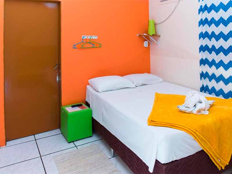 Quarto simples da São Jorge, dica de pousada em Bonito, com cama de casal e parede laranja