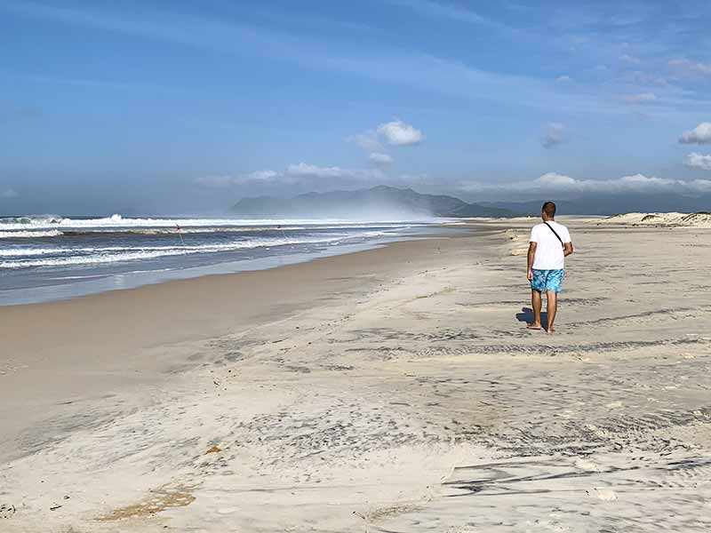 Homem caminha na praia da Guarda do Embaú em dia vazio de inverno