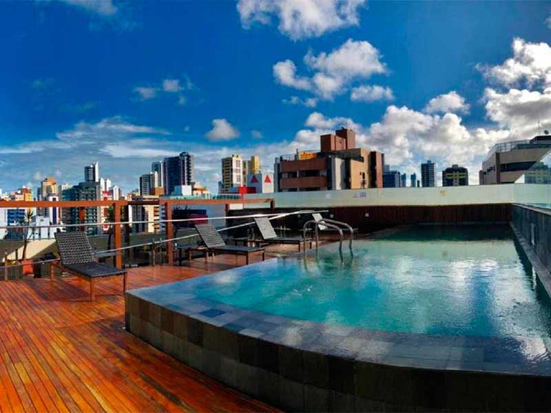 Piscina com espreguiçadeiras vazias do Hotel Manaíra e vista para os prédios