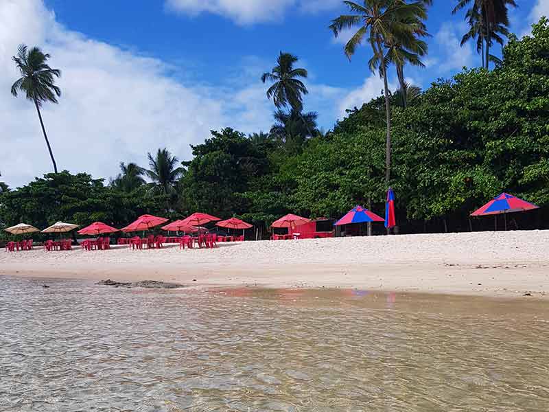 Água calma e transparente do mar de Coqueirinho com guarda-sóis na areia