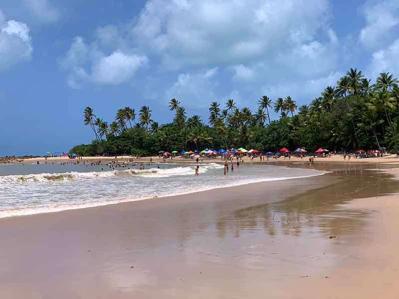 Pessoas se divertem no mar e na areia em dia de céu azul em Coqueirinho