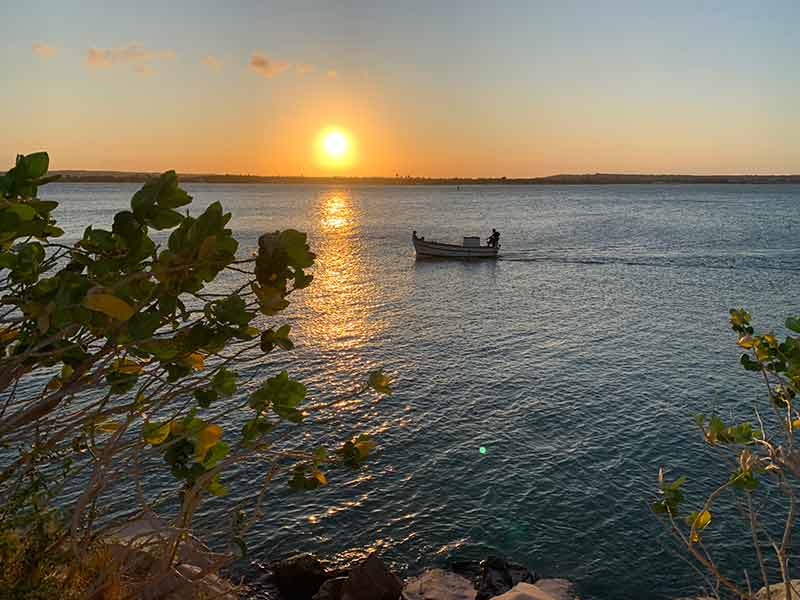 Barquinho navegando com sol se pondo no Dique de Cabedelo, na Paraíba