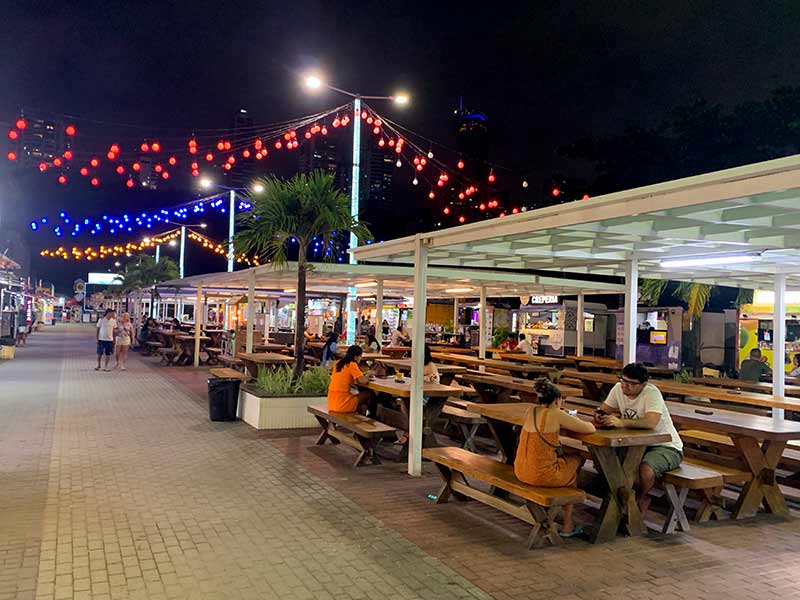 Pessoas sentadas em mesas compartilhadas e luzinhas penduradas no Parque Cabo Branco