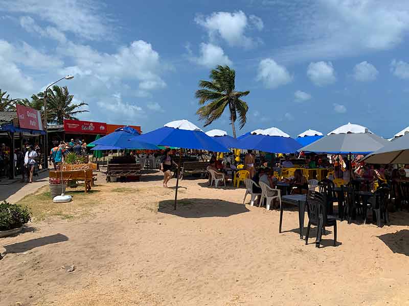 Praia de Coqueirinho lotada de barracas na areia em dia de céu com poucas nuvens