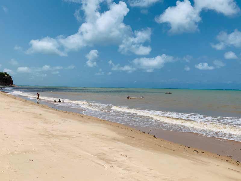 Areia vazia e mar com ondas em dia de céu azul com nuvens da Ponta do Seixas, dica de o que fazer em João Pessoa