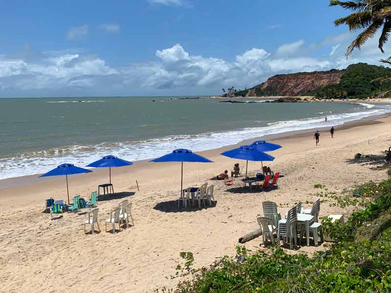 Pessoas sentadas na areia de Tabatinga, uma das melhores praias de João Pessoa, com guarda-sóis e mar vazio