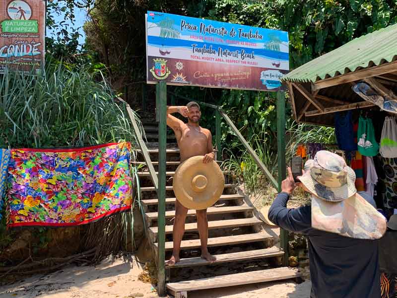 Homem com chapéu em frente ao corpo brinca na praia nudista de Tambaba