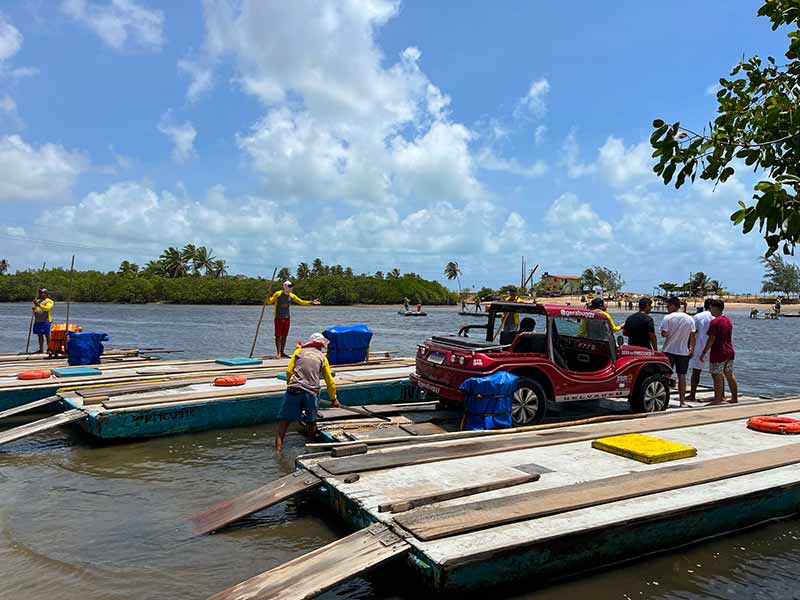 Buggy em balsa durante passagem pelo rio Ceará-Mirim em dia de céu com poucas nuvens