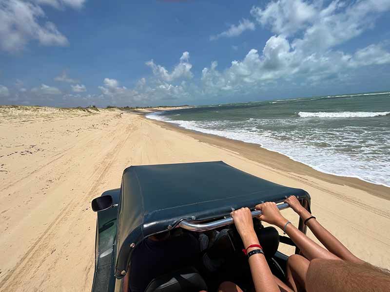 Pessoas se seguram em buggy na praia durante tour pelas Dunas de Genipabu, no Rio Grande do Norte