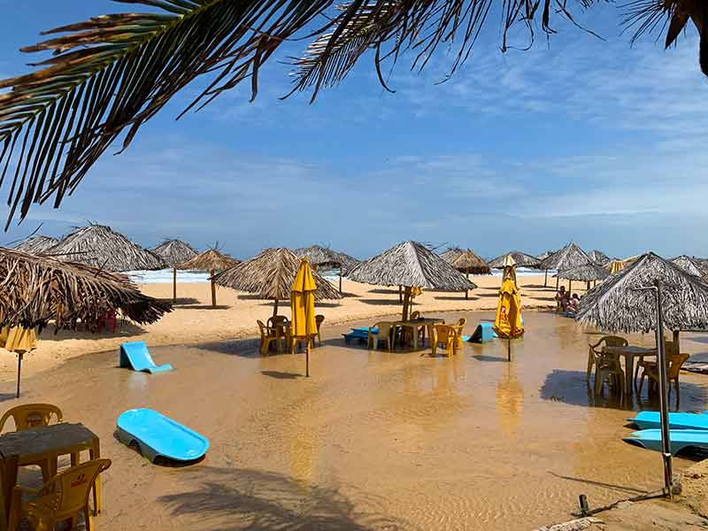 Mesas na areia com água e coqueiro em Búzios, praia de Natal