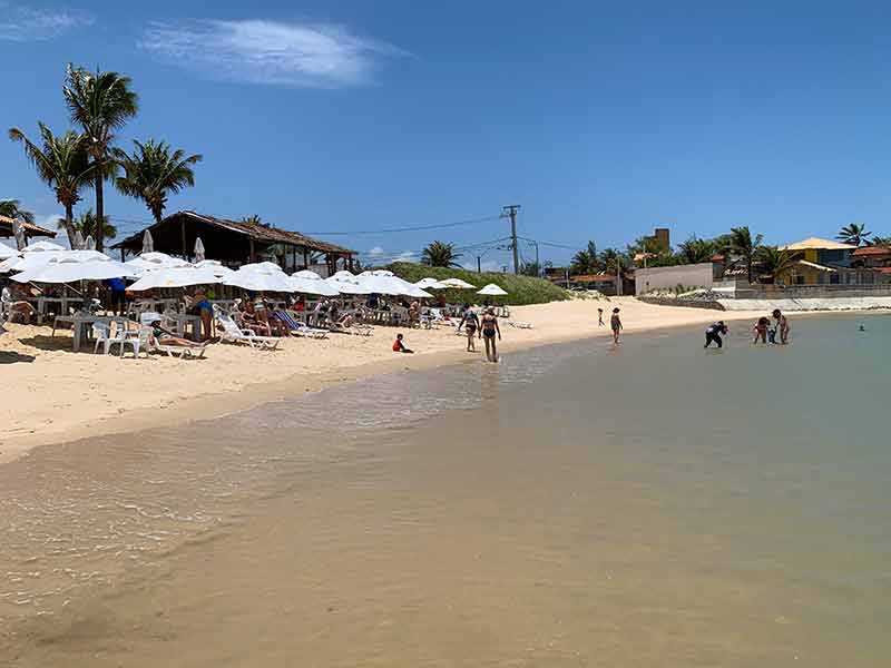 Guarda-sóis brancos na areia e pessoas no mar em Camurupim, uma das praias de Natal