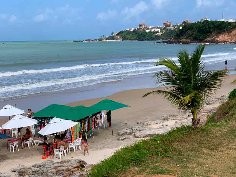 Pessoas na areia da Praia do Cotovelo, dica de o que fazer em Natal, vista de cima em dia de poucas nuvens