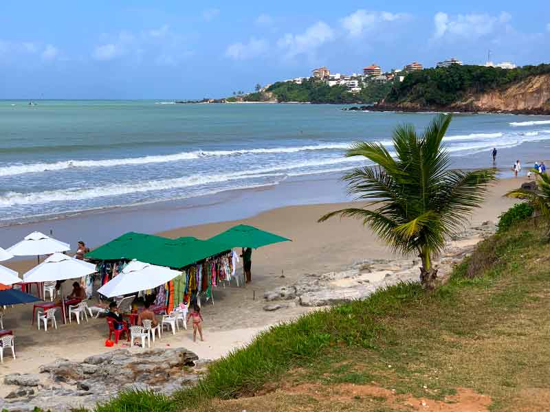 Vista de cima da praia do Cotovelo, perto de Natal, com mar vazio e guarda-sóis na areia