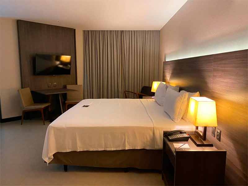 Quarto do Golden Tulip com cama de casal, TV e cortina fechada