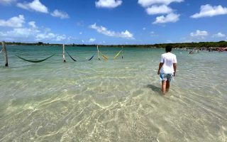 Lagoas em Natal: Homem caminha nas águas cristalinas da Lagoa do Carcará com redes coloridas ao fundo