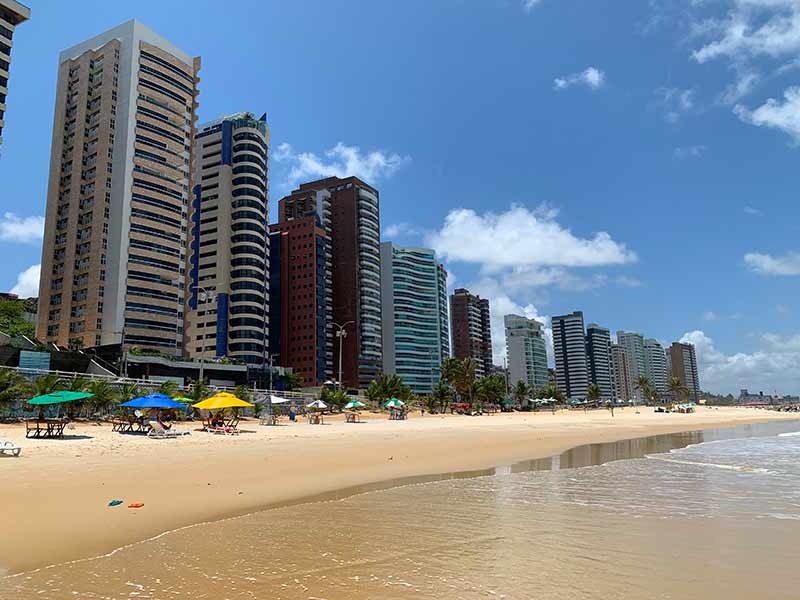 Grandes prédios na orla de Miami, praia de Natal, com guarda-sóis na areia e mar vazio