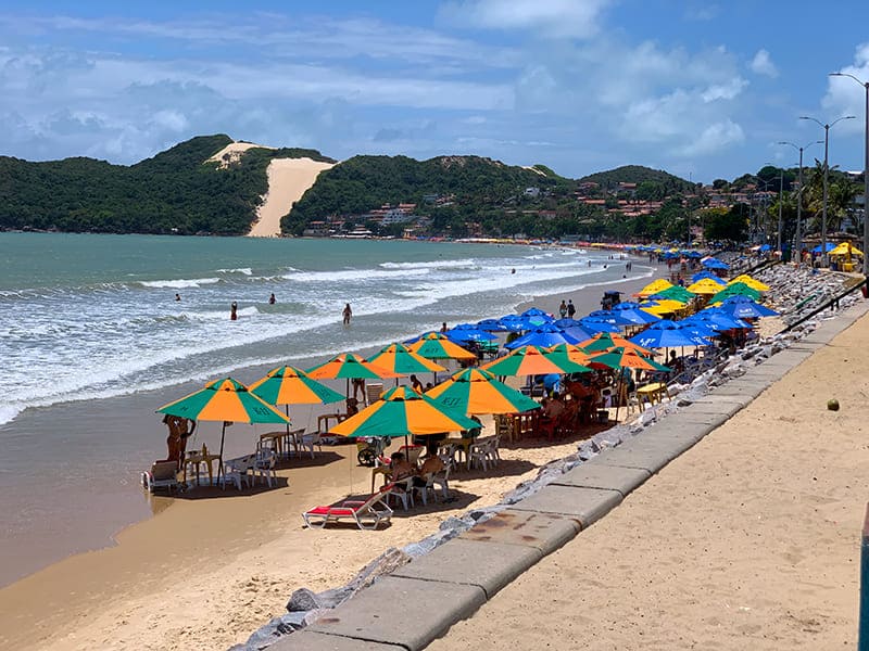 Guarda-sóis na praia de Ponta Negra com Morro do Careca ao fundo em dia de poucas nuvens