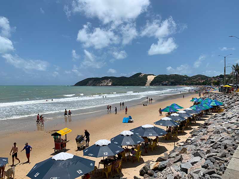 Pessoas na praia de Ponta Negra, dica do que fazer em Natal, com guardas-sóis na areia e mar vazio