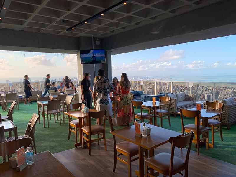 Área interna do Skybar, em João Pessoa, com pessoas sentadas em mesas