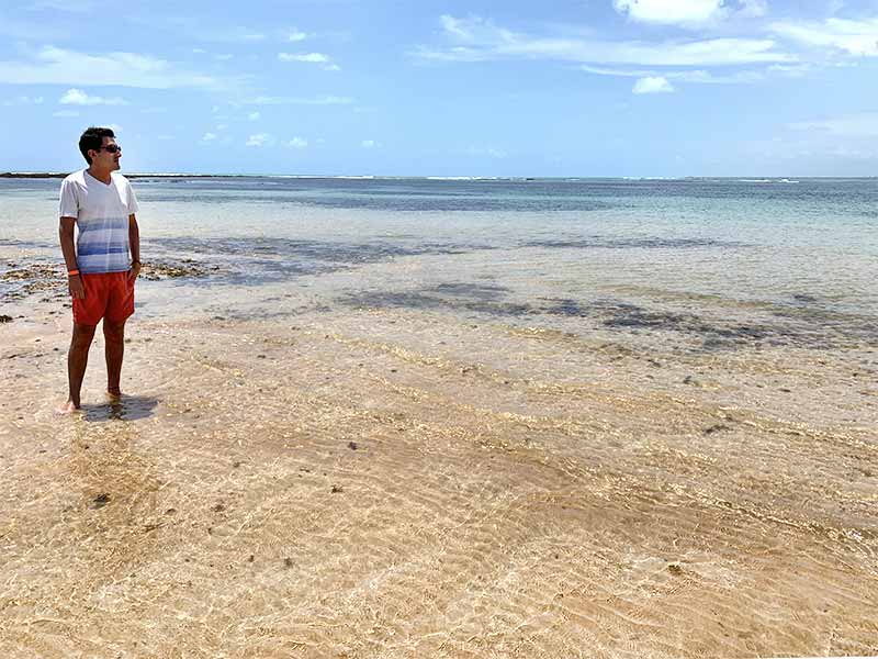 Homem em pé em banco de areia com águas cristalinas em Areia Vermelha