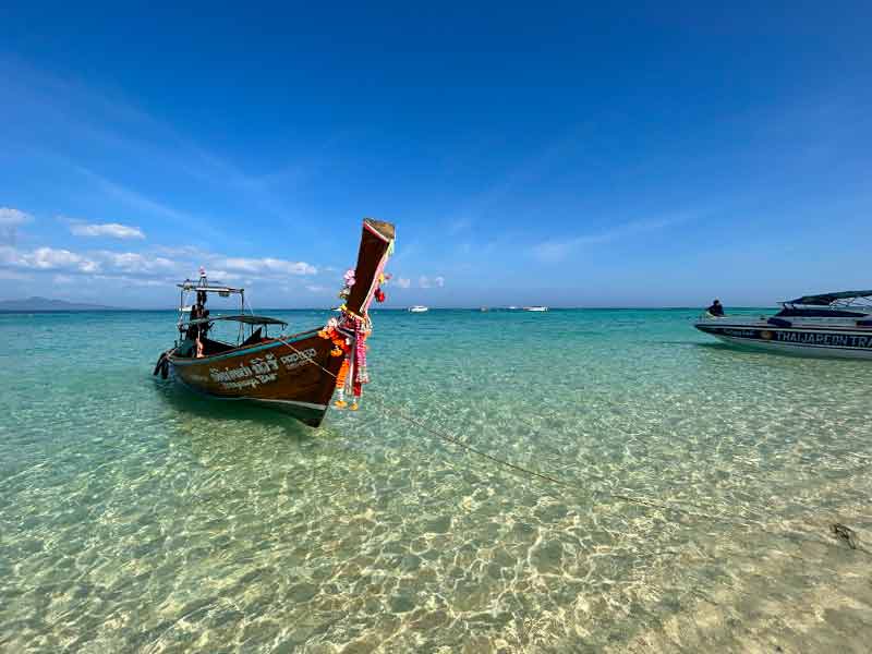 Barco long tail em águas cristalinas de Bamboo Island, na Tailândia, em dia de céu azul