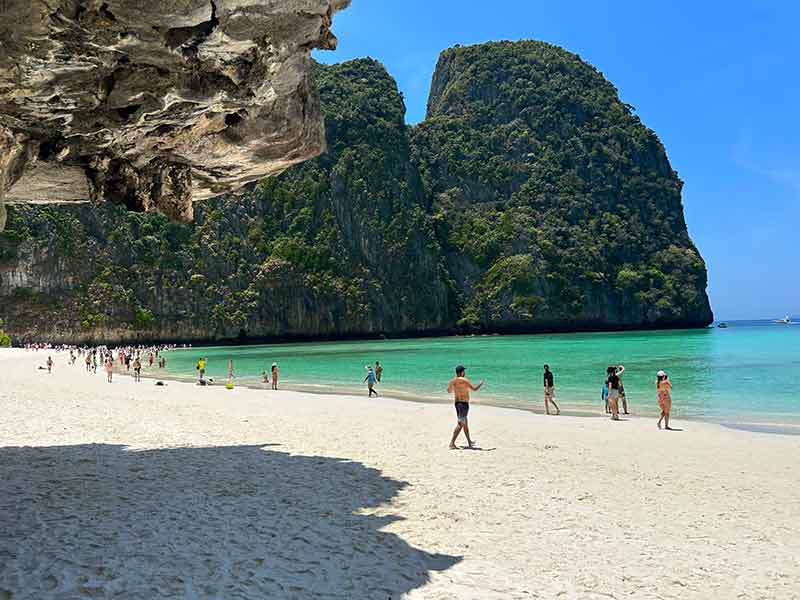 Pessoas na areia, mar esverdeado, pedras e céu azul em Maya Bay, dica de o que fazer em Phi Phi