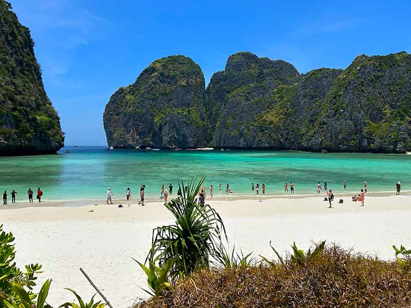 Pessoas nas areias de Maya Bay com mar esverdeado em dia de céu azul