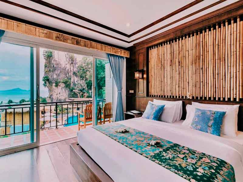 Quarto com cama de casal e varanda com decoração clara e de madeira do Railay Phutawan Resort