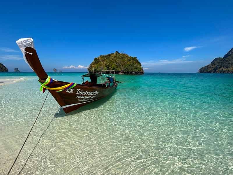 Mar esverdeado e cristalino da Tup Island, perto de Railay Beach, com barco parado em dia de céu azul