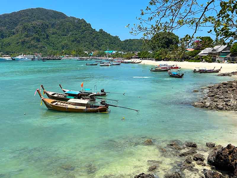 Mar esverdeado e claro com barco em dia de céu azul em ilha na Tailândia