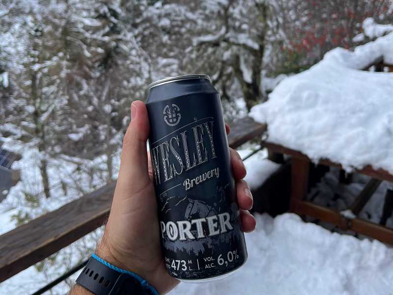 Mão segurando lata de cerveja porter da Wesley com fundo de neve