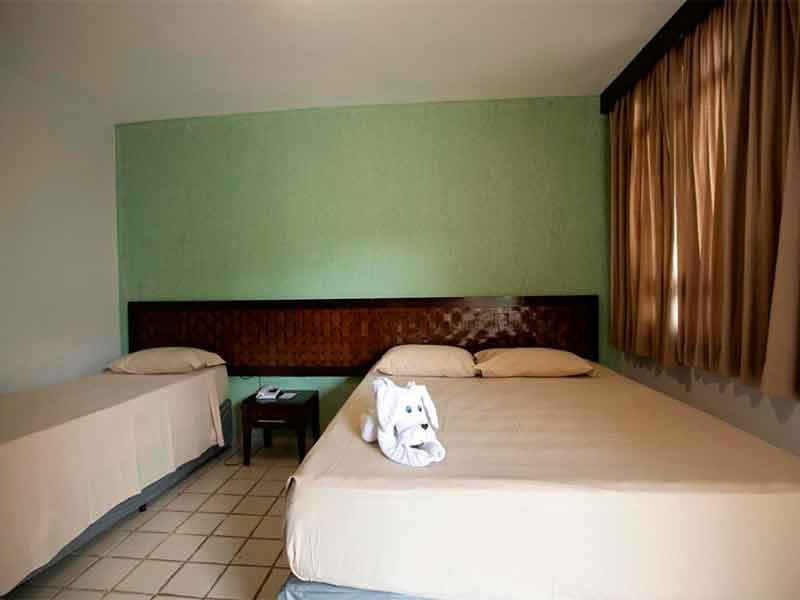 Quarto simples do Eco Chalés com cama de casal e cama de solteiro e parede verde