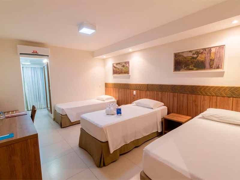 Quarto do Hotel Turismo, dica de onde ficar em Rio Quente, com três camas de solteiro, quadro na parede e mesa de trabalho