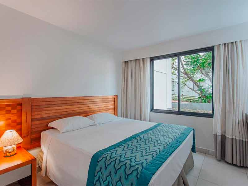 Quarto do hotel Luupi com cama de casal, abajur e janela com cortina