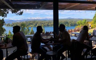 Pessoas almoçam e bebem com vista pro lago e montanhas na Cervejaria Patagonia