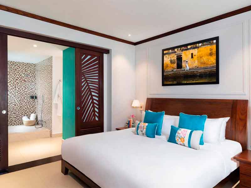 Quarto do Anantara, dica de hotel em Hoi An, com cama de casal, almofadas azuis, quadro e banheiro ao fundo