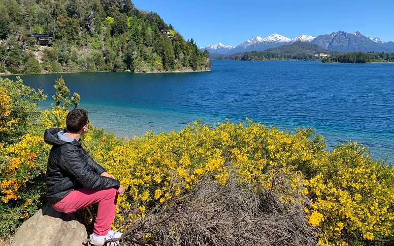 Homem sentado observa lago e montanha com neve em Bariloche