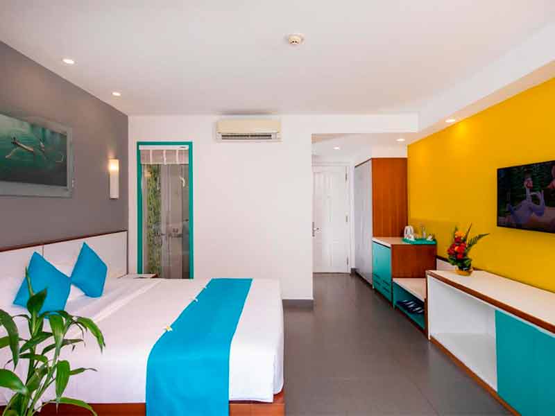 Quarto do ÊMM Hotel, dica de onde ficar em Hoi An, com decoração azul e amarela, cama, TV e ar-condicionado