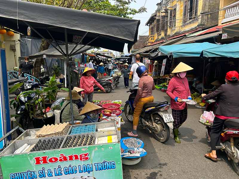 Motos passam entre barracas em feira livre, dica de o que fazer em Hoi An