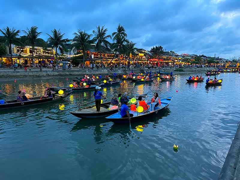 Barcos com lanternas acesas passeiam pelo rio em Hoi An no fim da tarde