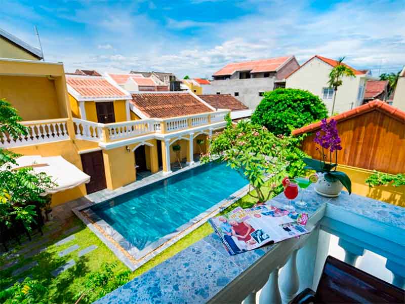 Vista da varanda do Hoian Central, dica de onde ficar em Hoi An, com piscina vazia e prédio amarelo em dia de céu azul com poucas nuvens