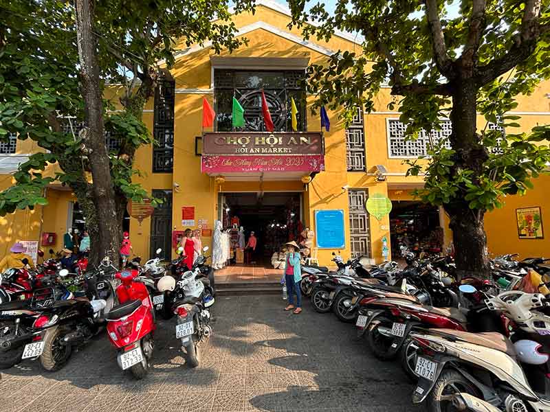 Entrada do Mercado de Hoi An, prédio amarelo com diversas motos estacionadas na frente