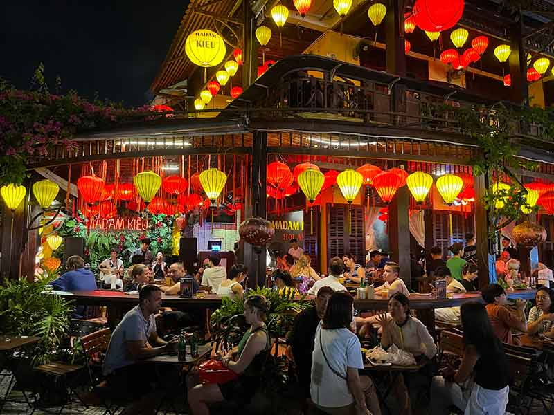 Pessoas sentadas em mesas em bar com lanternas acesas, dica de o que fazer em Hoi An à noite