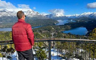 Homem observa montanhas com neve e lago no Cerro Campanário, no Circuito Chico, em Bariloche